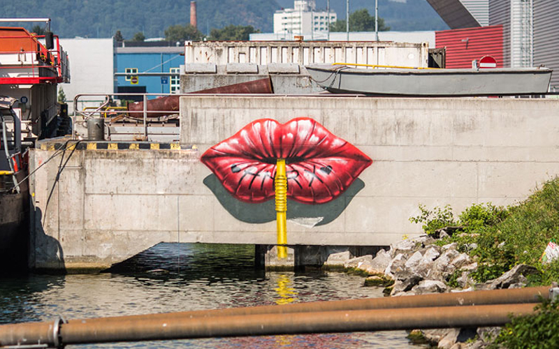 Wandbild roter Lippen auf einer Betonmauer am Wasser im Linzer Hafen